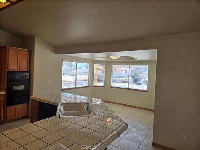 kitchen featuring plenty of natural light, sink, tile counters, and black oven