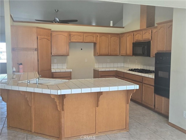 kitchen featuring tile counters, ceiling fan, a kitchen island, black appliances, and a sink