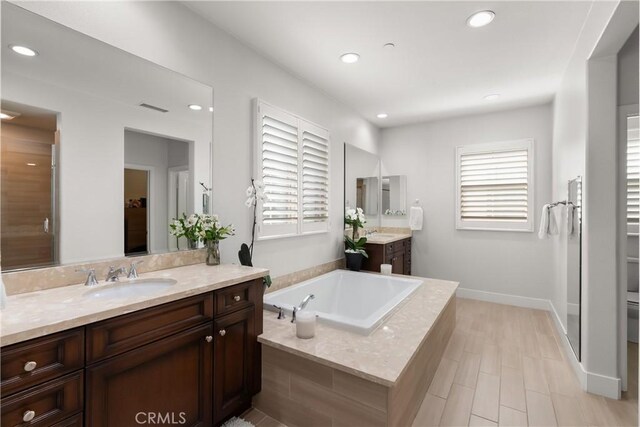 bathroom featuring vanity, plenty of natural light, a relaxing tiled tub, and toilet