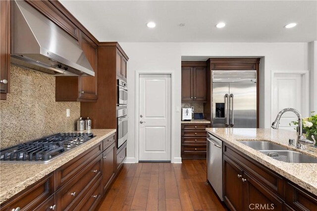 kitchen with extractor fan, appliances with stainless steel finishes, sink, light stone counters, and dark wood-type flooring