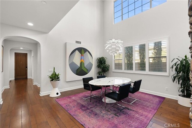 dining area with a notable chandelier, a towering ceiling, and dark wood-type flooring