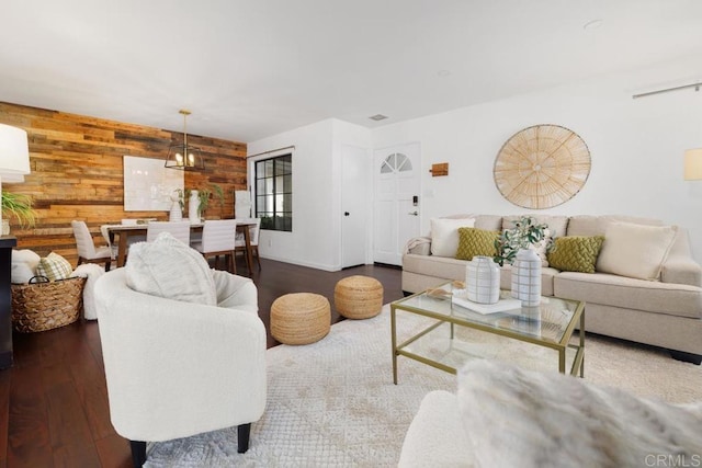 living room featuring wooden walls, a notable chandelier, and dark hardwood / wood-style flooring