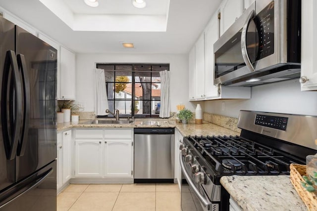 kitchen with white cabinetry, sink, light stone counters, a tray ceiling, and stainless steel appliances