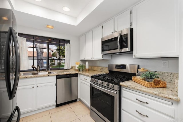 kitchen with a raised ceiling, sink, white cabinets, light stone counters, and stainless steel appliances