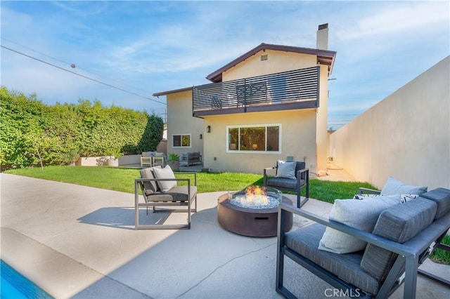 rear view of property featuring a patio, a balcony, an outdoor living space with a fire pit, and a lawn