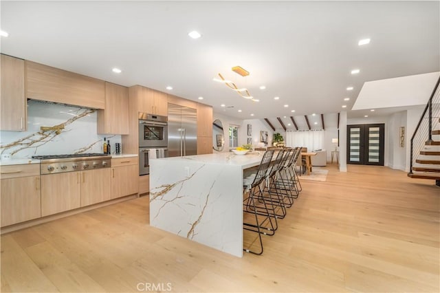 kitchen with light stone countertops, stainless steel appliances, a spacious island, and light brown cabinets