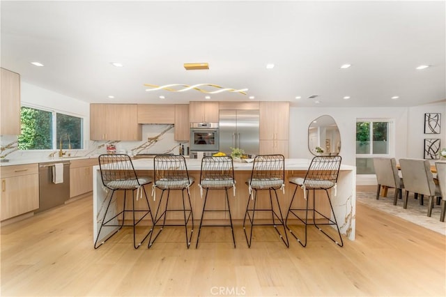 kitchen featuring stainless steel appliances, a kitchen breakfast bar, light brown cabinetry, and an island with sink