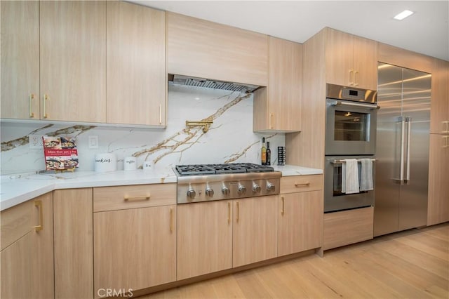 kitchen with stainless steel appliances, light stone counters, light brown cabinetry, decorative backsplash, and light wood-type flooring