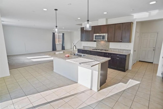 kitchen with sink, appliances with stainless steel finishes, a kitchen island with sink, light stone counters, and decorative light fixtures