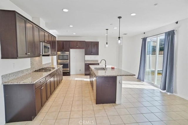 kitchen featuring pendant lighting, sink, stainless steel appliances, light stone counters, and a center island with sink