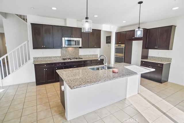 kitchen featuring pendant lighting, sink, a kitchen island with sink, light stone counters, and stainless steel appliances