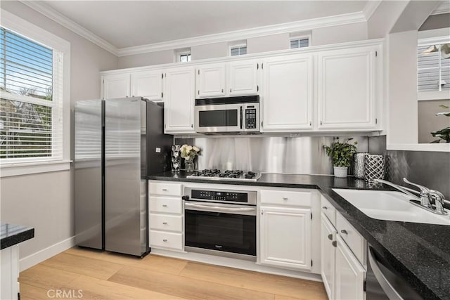 kitchen featuring sink, crown molding, white cabinetry, stainless steel appliances, and dark stone counters