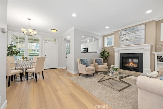 living room with crown molding, a notable chandelier, a tiled fireplace, and light wood-type flooring