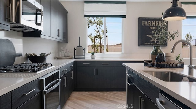 kitchen featuring sink, stainless steel appliances, hanging light fixtures, and light wood-type flooring