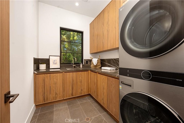 clothes washing area with stacked washer / dryer, dark tile patterned floors, sink, and cabinets