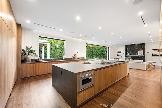 kitchen featuring sink, light hardwood / wood-style floors, stainless steel gas cooktop, and a spacious island