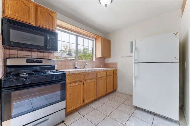 kitchen with stainless steel gas range oven, light tile patterned floors, tile counters, white fridge, and backsplash