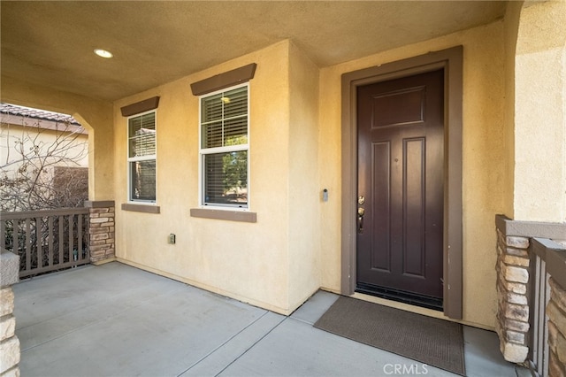 doorway to property featuring stone siding, a porch, and stucco siding