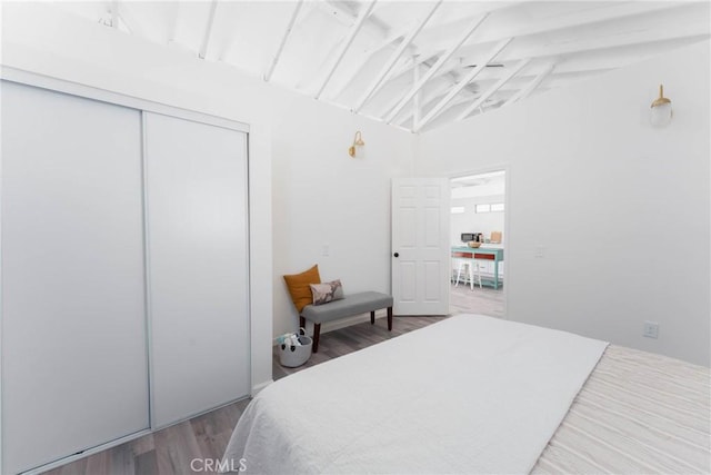 bedroom with hardwood / wood-style floors, lofted ceiling with beams, and a closet