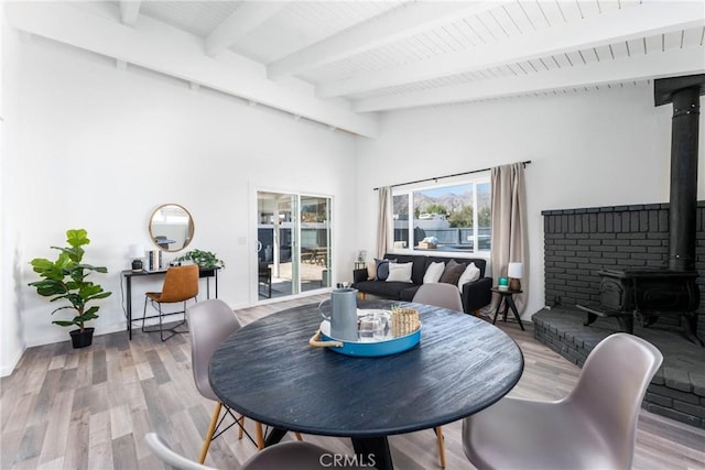 dining space featuring vaulted ceiling with beams, wood-type flooring, wooden ceiling, and a wood stove