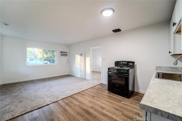 kitchen featuring a wall mounted air conditioner, sink, white cabinets, light hardwood / wood-style floors, and black gas range