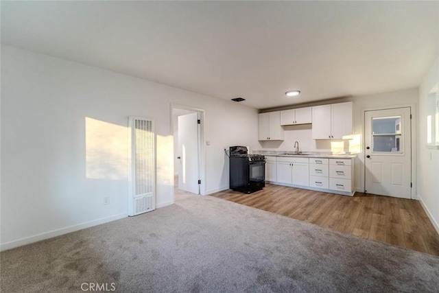 kitchen with black gas range oven, sink, white cabinetry, and light colored carpet