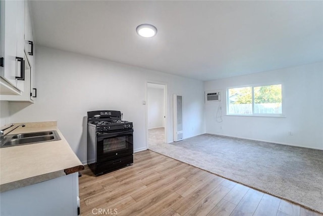 kitchen featuring black range with gas cooktop, white cabinetry, sink, a wall unit AC, and light hardwood / wood-style flooring