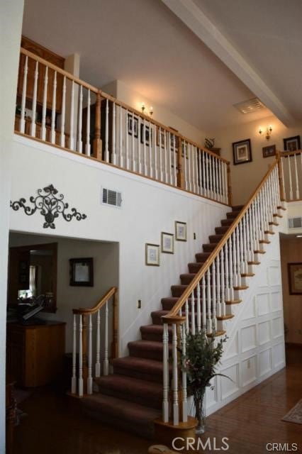 stairs featuring beamed ceiling, a towering ceiling, and hardwood / wood-style floors