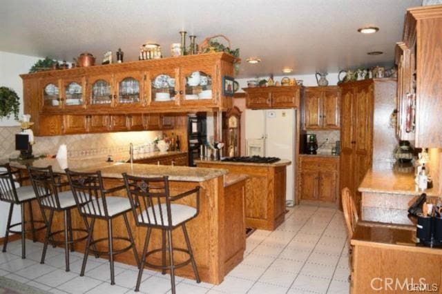 kitchen with a breakfast bar, white refrigerator with ice dispenser, kitchen peninsula, and decorative backsplash