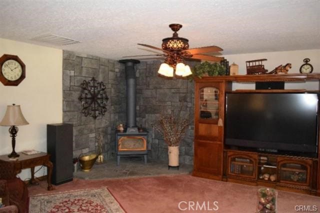 living room featuring ceiling fan, a wood stove, and a textured ceiling