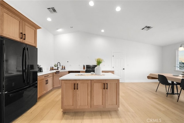 kitchen with vaulted ceiling, sink, a center island, black appliances, and light hardwood / wood-style flooring