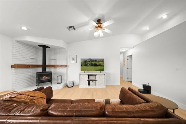 living room with lofted ceiling, light hardwood / wood-style flooring, ceiling fan, and a wood stove