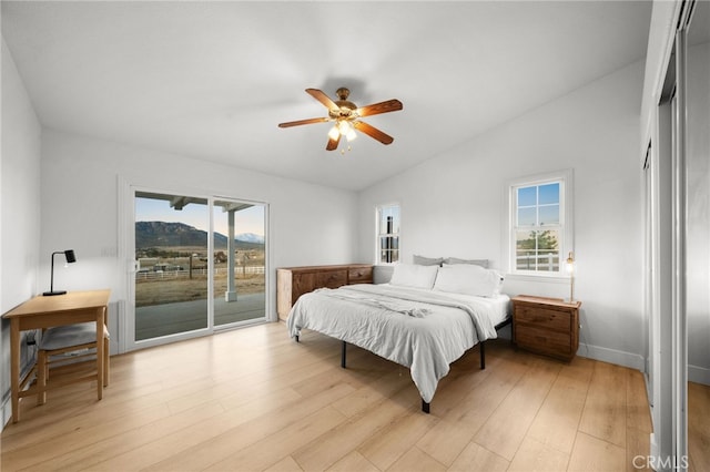 bedroom with vaulted ceiling, multiple windows, access to outside, a mountain view, and light hardwood / wood-style flooring