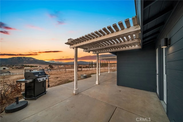 patio terrace at dusk with area for grilling, a pergola, and a mountain view