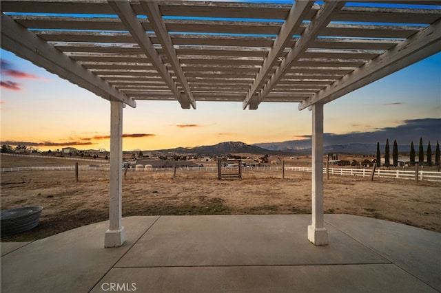 patio terrace at dusk with a mountain view, a rural view, and a pergola