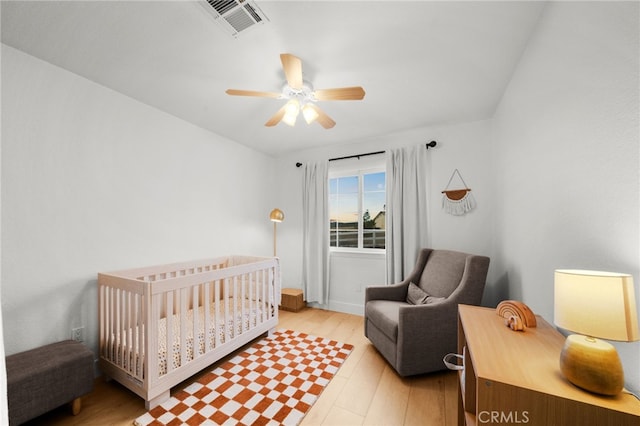 bedroom with a crib, light hardwood / wood-style floors, and ceiling fan