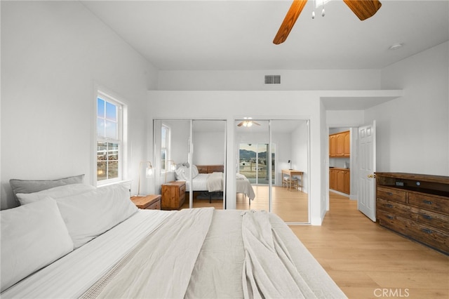 bedroom with ceiling fan, light hardwood / wood-style floors, and multiple closets