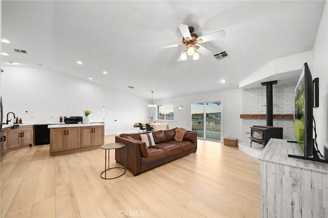 living room with vaulted ceiling, a wood stove, ceiling fan, and light wood-type flooring