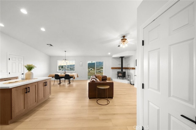 living room with ceiling fan with notable chandelier, vaulted ceiling, light hardwood / wood-style floors, and a wood stove