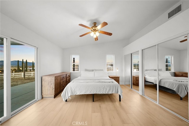 bedroom featuring vaulted ceiling, two closets, access to exterior, ceiling fan, and light hardwood / wood-style flooring