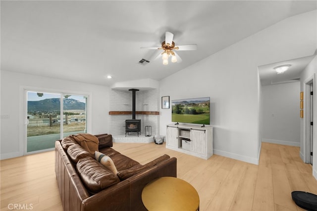 living room with light wood-type flooring, vaulted ceiling, ceiling fan, and a wood stove