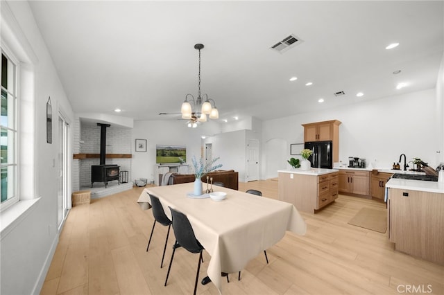 dining space with a wood stove, a chandelier, and light wood-type flooring