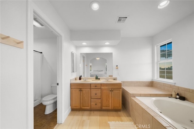 bathroom featuring tiled tub, vanity, and toilet