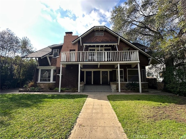 view of front facade featuring a front lawn, a balcony, and a chimney