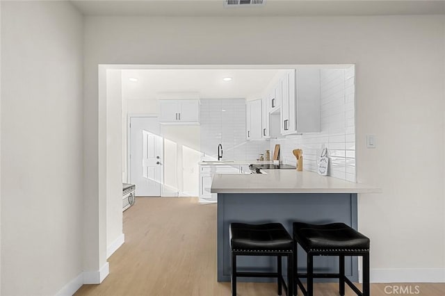 interior space featuring a breakfast bar area, tasteful backsplash, light countertops, white cabinetry, and a sink