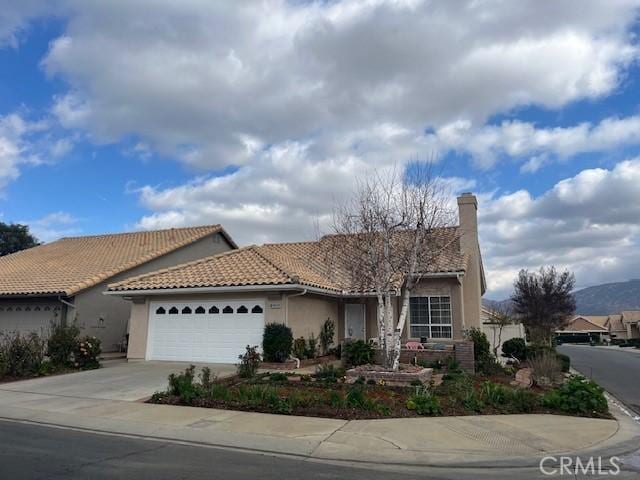 single story home with a chimney, stucco siding, concrete driveway, an attached garage, and a tiled roof