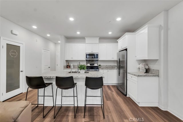 kitchen with a kitchen island with sink, stainless steel appliances, dark wood-type flooring, white cabinetry, and light stone countertops