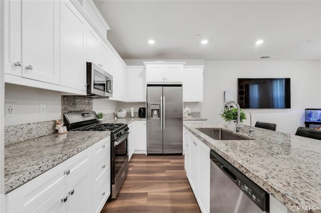 kitchen with sink, white cabinetry, dark hardwood / wood-style flooring, stainless steel appliances, and light stone countertops