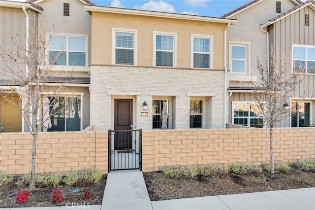 townhome / multi-family property featuring a fenced front yard, a gate, stone siding, and stucco siding