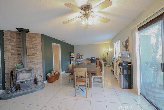 dining area featuring a textured ceiling, a wood stove, ceiling fan, and light tile patterned flooring